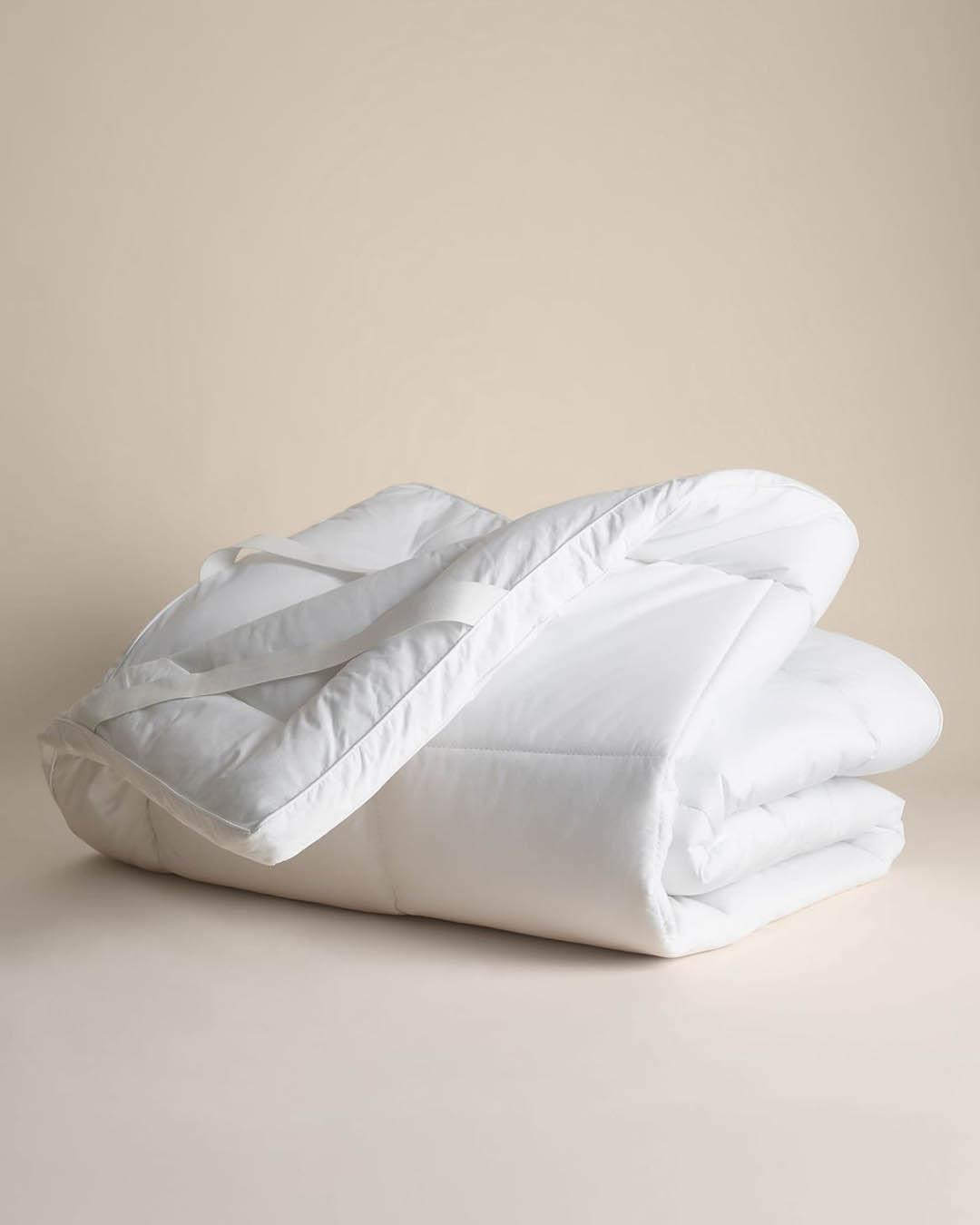 Folded white duvet with corner straps on neutral background — soft, breathable quilt for bed, hotel-style warmth and comfort