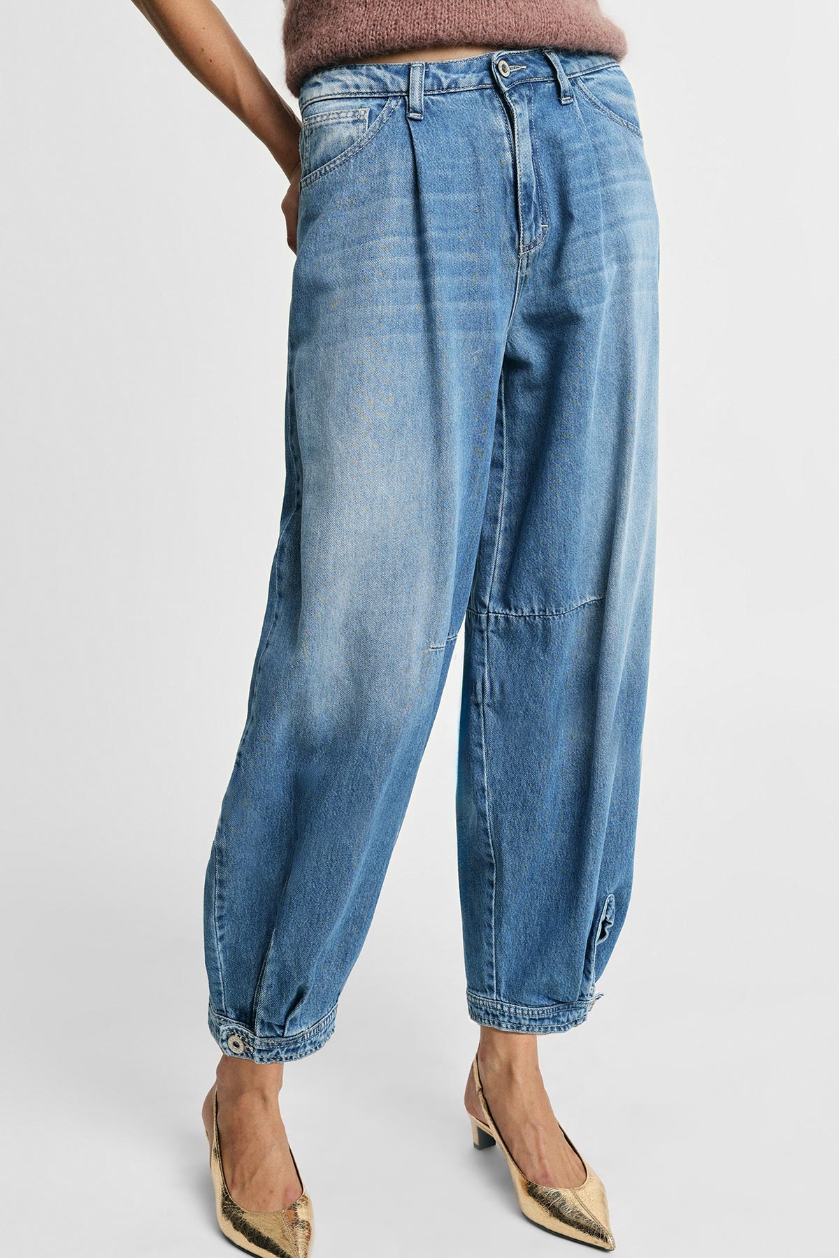 Women's relaxed high-waist faded blue denim trousers with tapered legs and buttoned elasticated cuffs, worn with gold heels