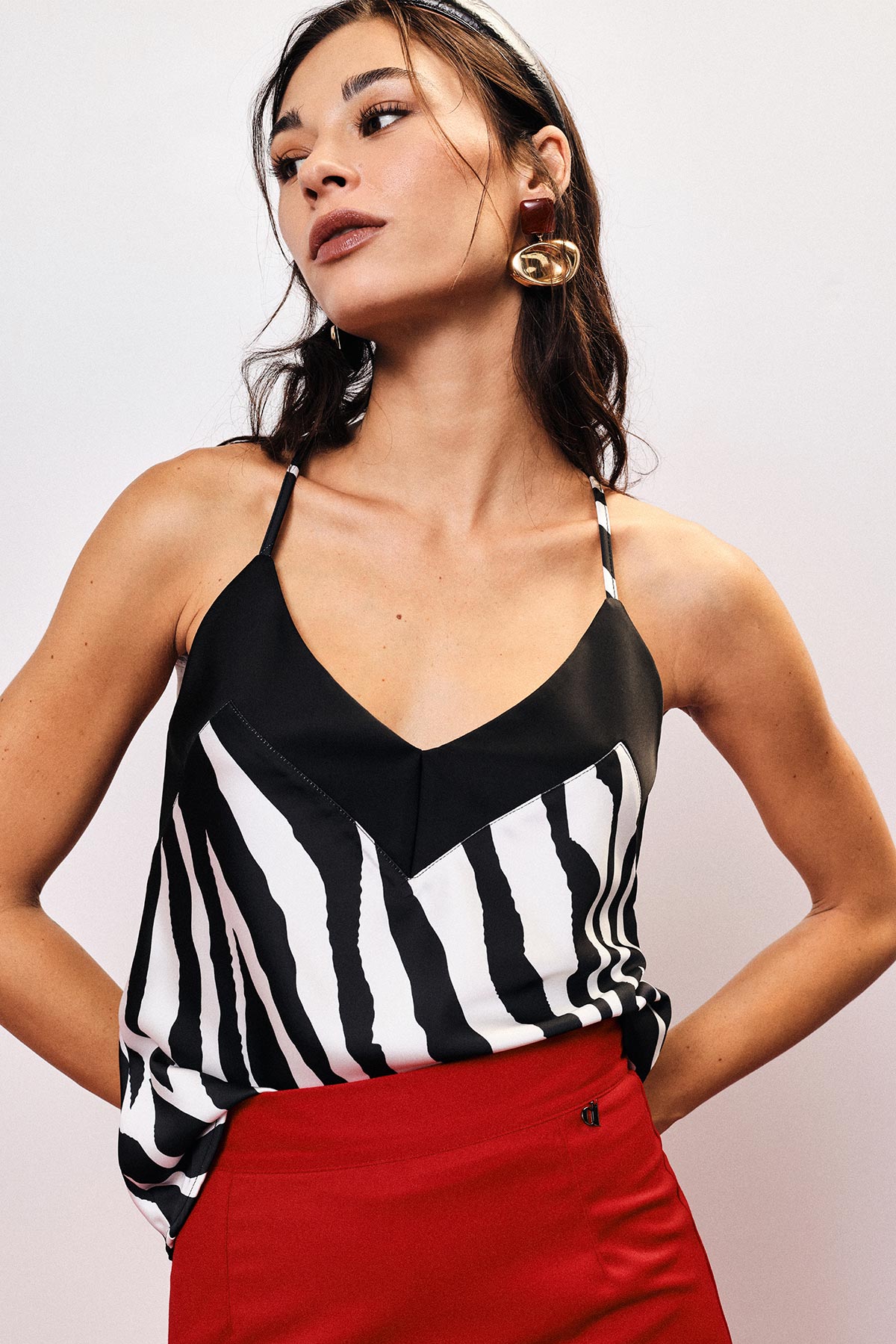 Woman wearing zebra-print black-and-white camisole and red skirt, posing with hands on hips and gold statement earring