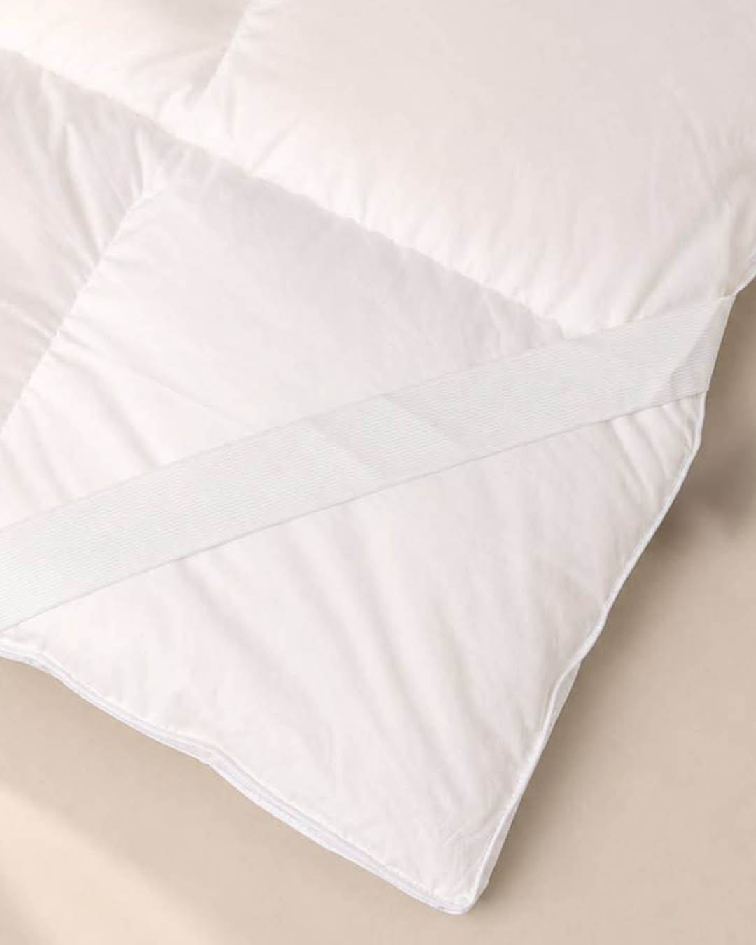 White quilted mattress topper corner with elastic securing strap on beige background