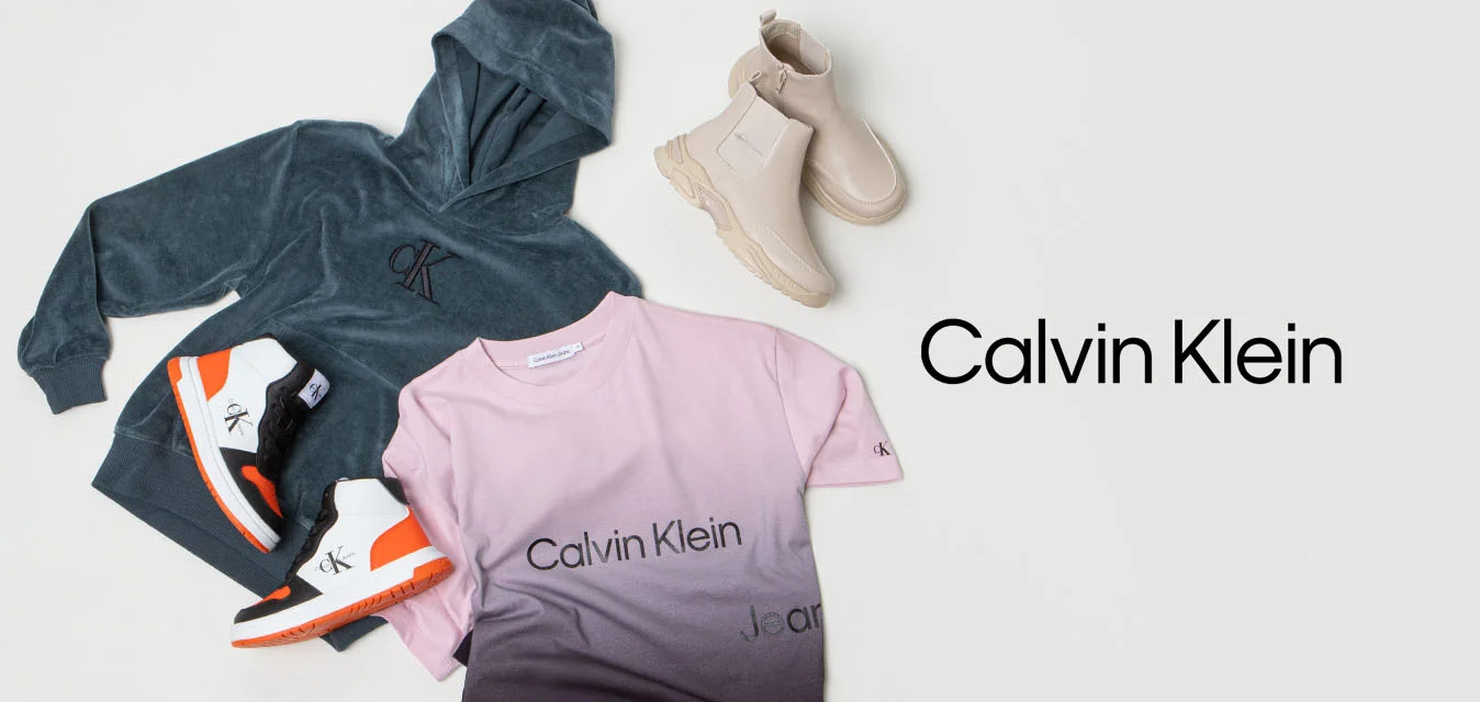 Felpa grigia, t-shirt a gradiente rosa con logo, sneakers neri e arancioni e stivaletti beige, tutti presentati su uno sfondo bianco.