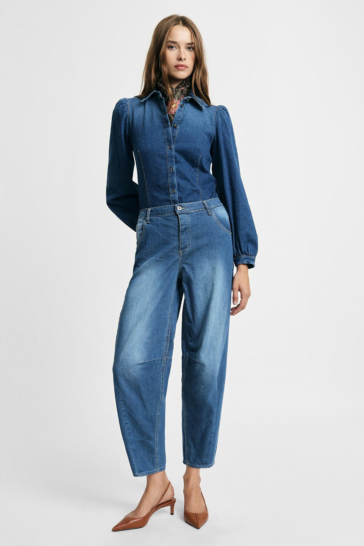 Woman modelling denim button-up blouse with puffed sleeves and high‑waist relaxed jeans, brown heels, studio background