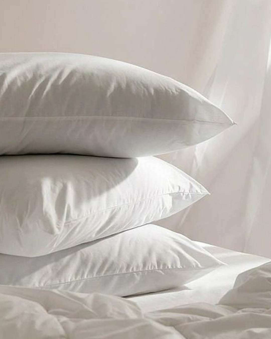 Stack of three white pillows on a neatly made bed with crisp cotton covers, soft natural light highlighting smooth bedding