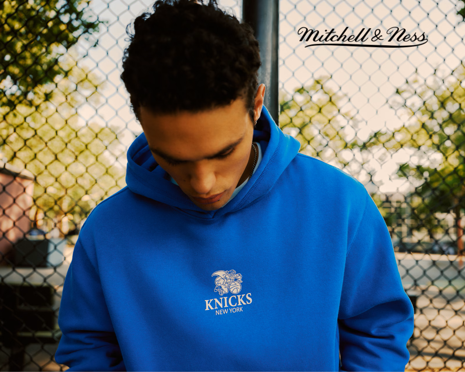 Model wears blue New York Knicks Mitchell & Ness hoodie.
