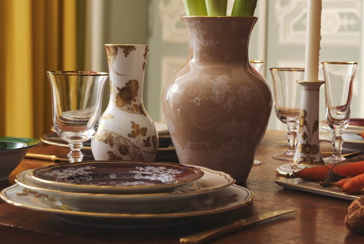 Elegant dining table with stacked vintage china plates, decorative vases, crystal glasses and a tapered candle in a gilt holder