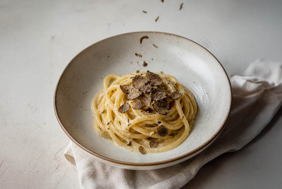 Creamy spaghetti pasta topped with shaved black truffle in a rustic bowl on a white linen cloth