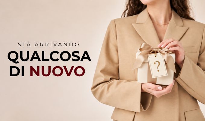Woman in beige blazer holding small wrapped gift with question-mark tag beside Italian text 'Sta arrivando qualcosa di nuovo'