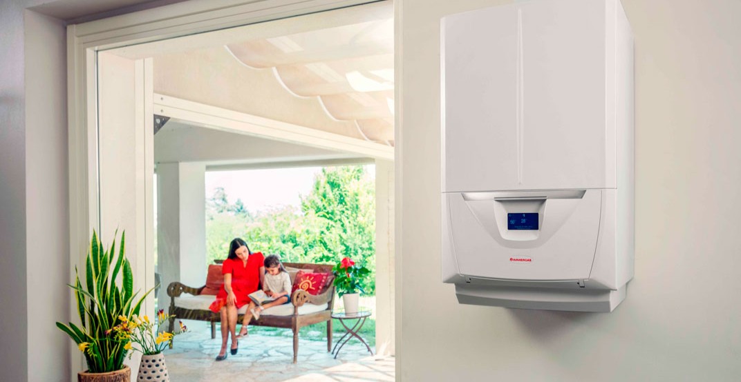 Wall-mounted white condensing boiler with digital display in a bright home, patio visible with a woman and child reading on a bench