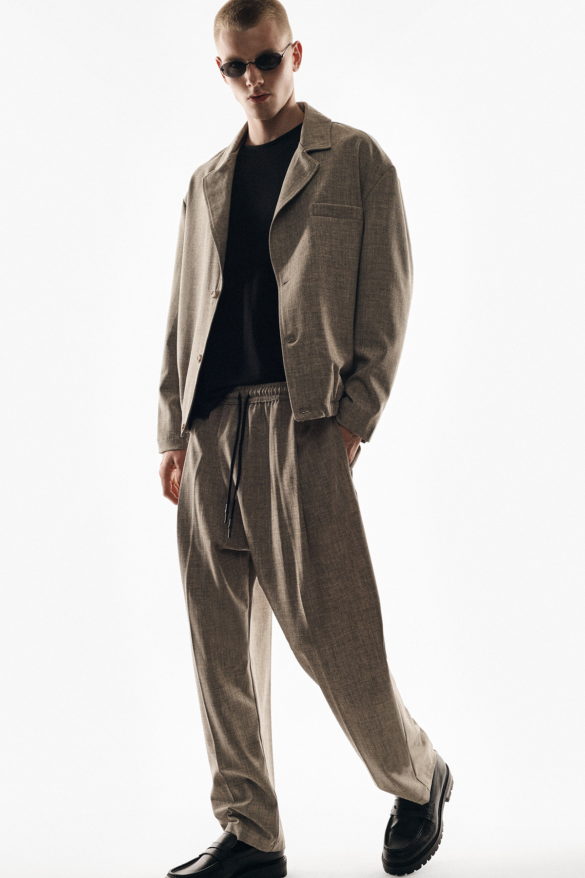 Young man in relaxed beige blazer and drawstring wide-leg trousers with black tee and sunglasses, minimalist menswear fashion lookbook