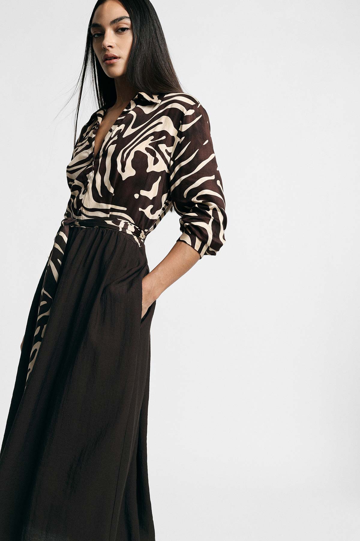 Woman modelling long dark skirt and brown-and-cream abstract zebra-print blouse with hand in pocket, studio fashion portrait