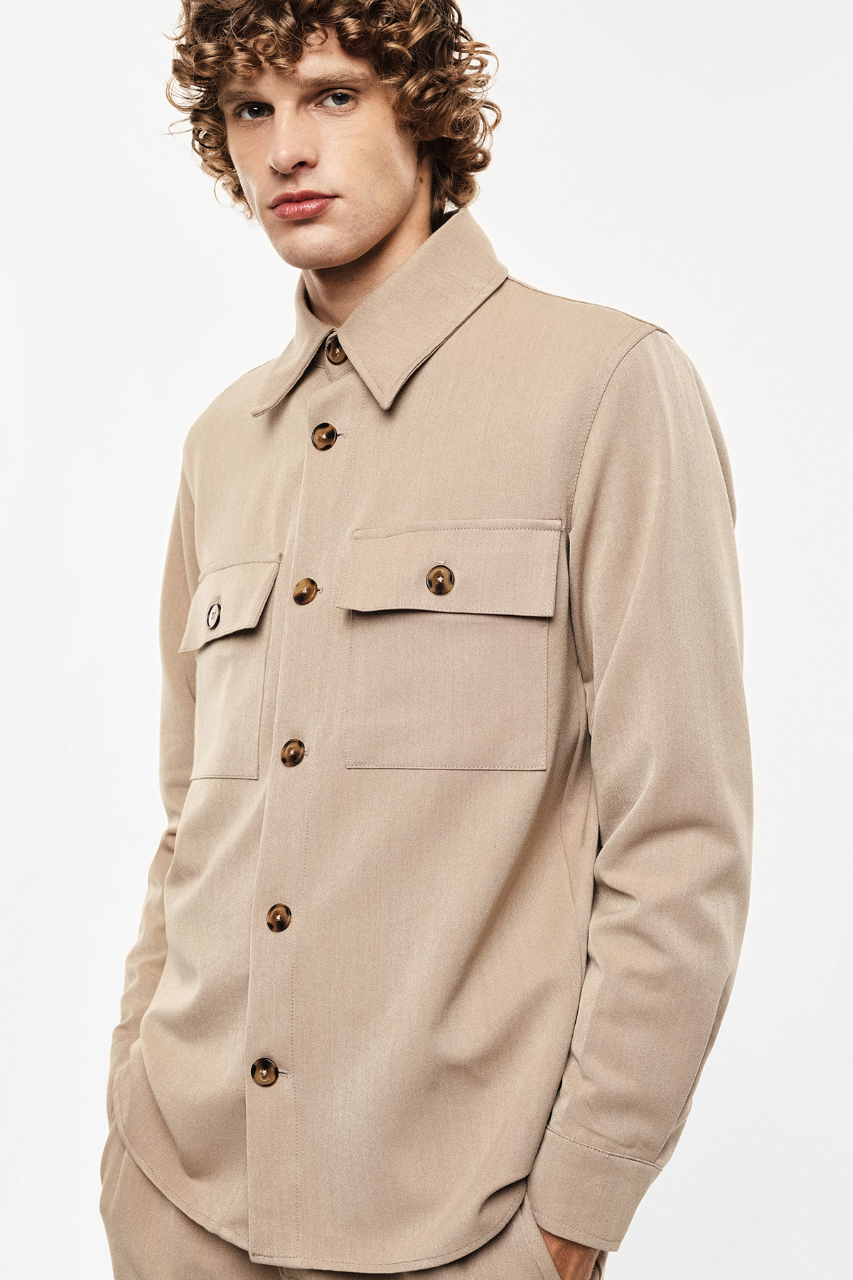 Man wearing beige button-up overshirt with chest flap pockets, long sleeves and tortoiseshell buttons