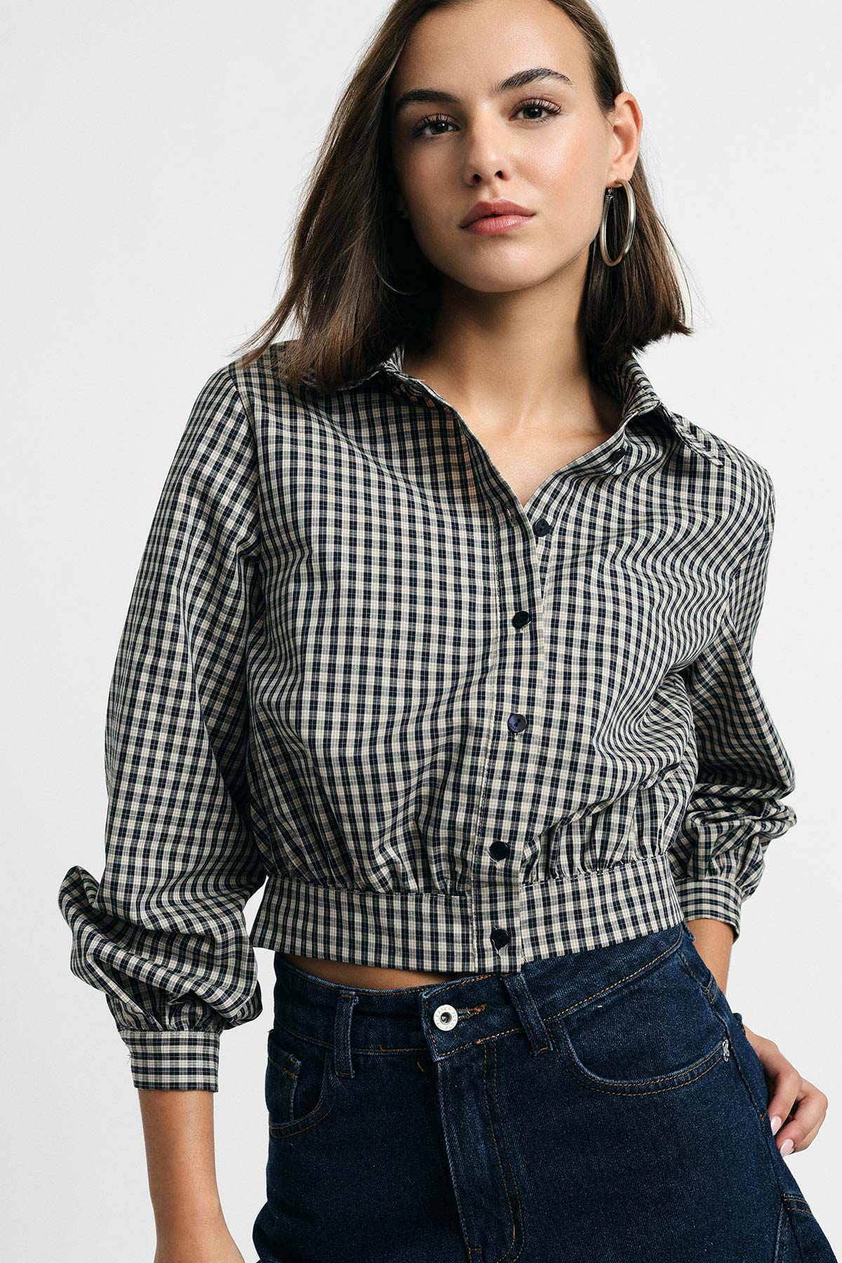 Woman modelling cropped black-and-white gingham button-up shirt with cinched waist and high-waisted dark denim jeans
