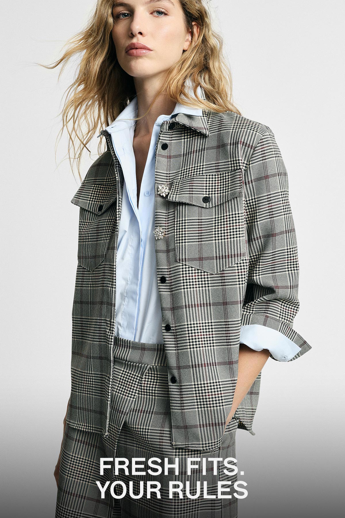 Woman wearing grey checked jacket and matching trousers over a light blue shirt, hands in pockets; 'Fresh fits. Your rules.'