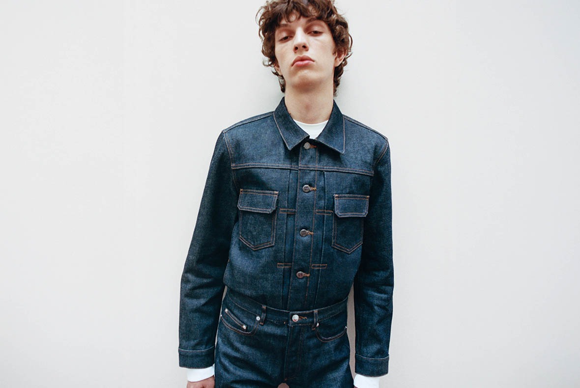 Young person in matching dark blue denim jacket and high-waisted jeans with chest pockets, standing against a white background