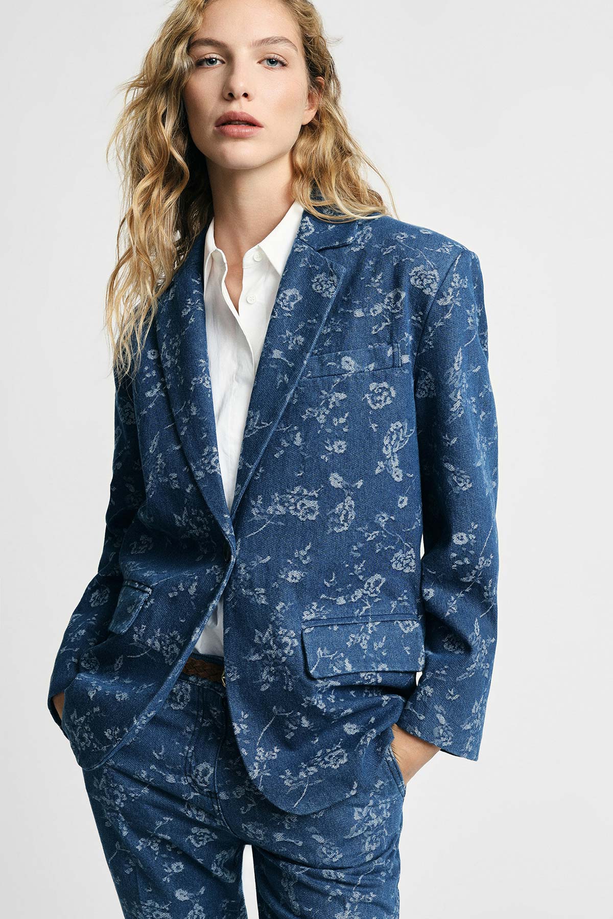 Woman wearing a blue floral-patterned blazer and matching trousers with a white shirt, hands in pockets, fashion portrait