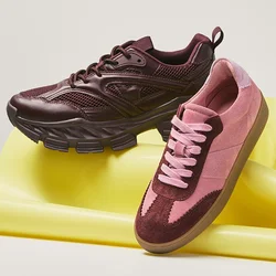 Coppia di sneakers bordeaux e rosa appoggiate su un tappetino da ginnastica giallo piegato su uno sfondo semplice.