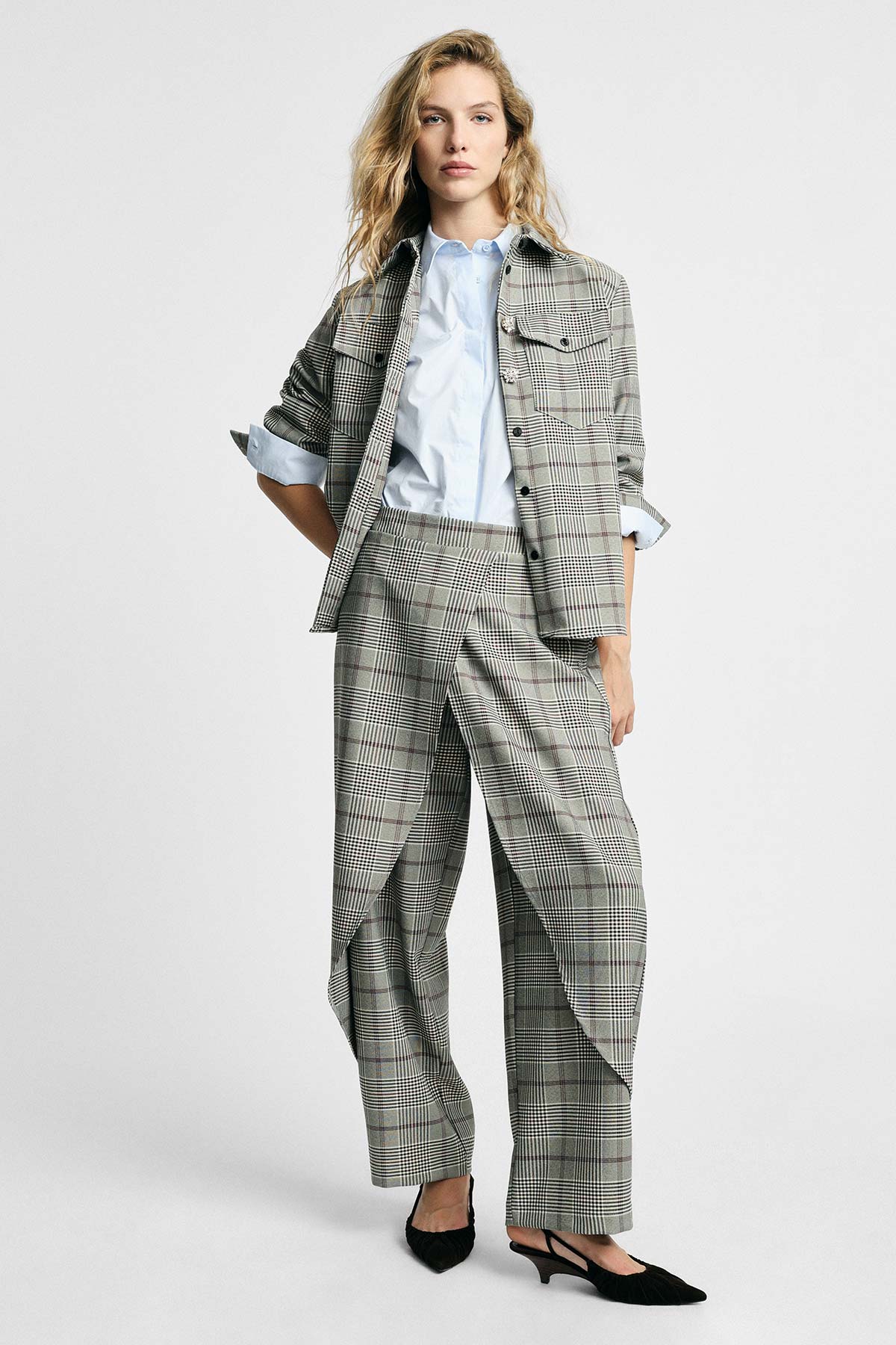 Female model in grey checked jacket and wide-leg trousers, light blue shirt and black kitten heels on white background