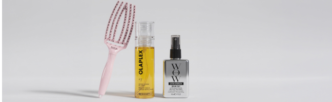 Scatto pubblicitario di tre prodotti per la cura dei capelli con spazzola rosa, olio per capelli Olaplex e Colow Wow Spray.