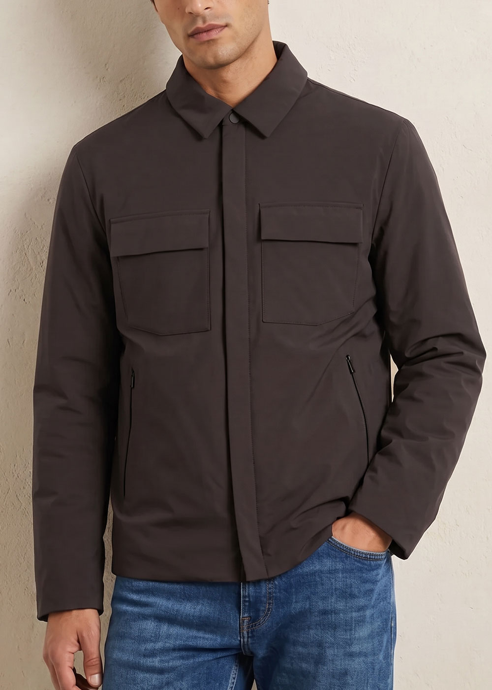 Man wearing dark charcoal men's jacket with flap chest pockets, zip side pockets and collar, hand in blue jeans pocket