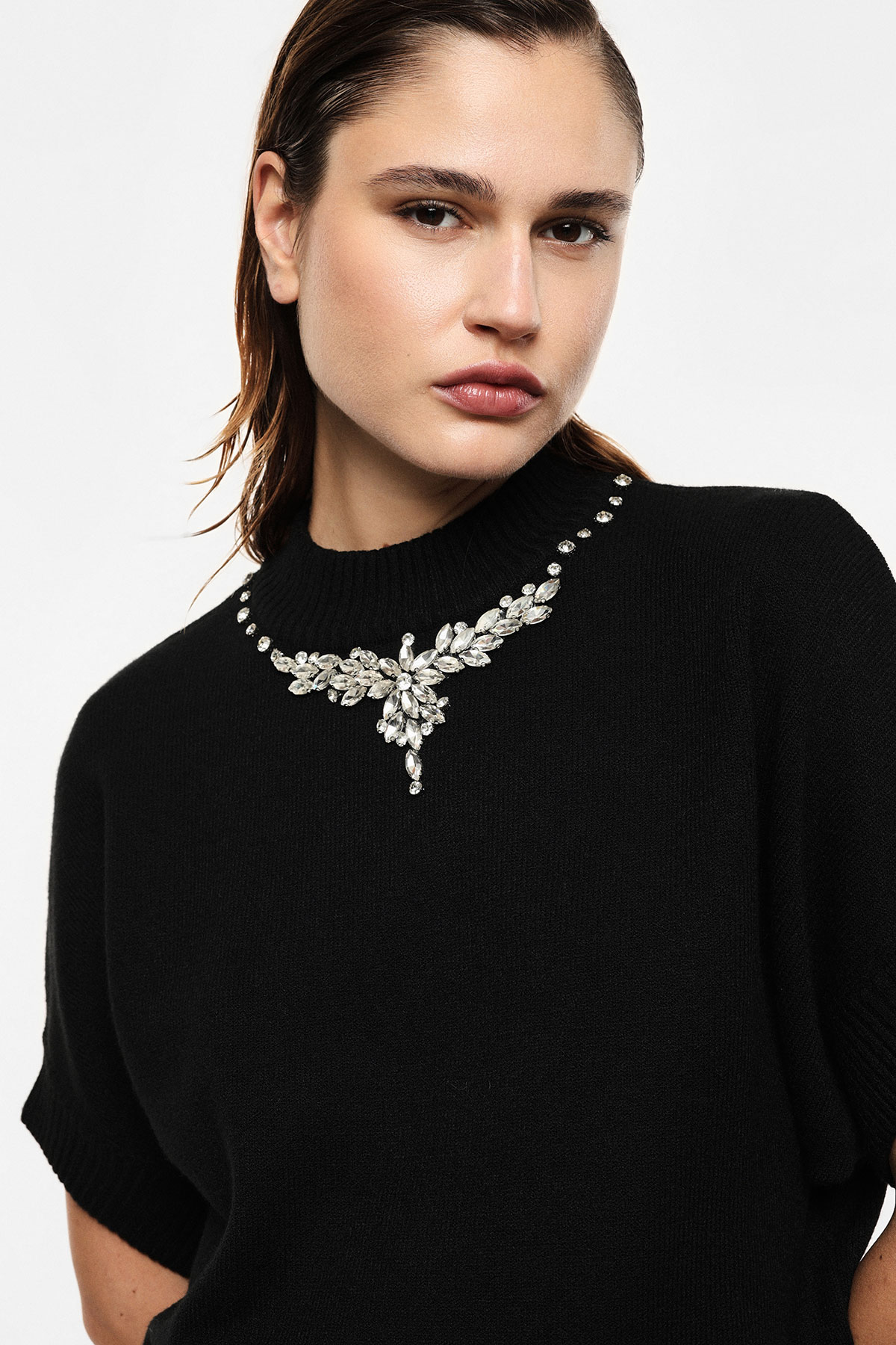 Close-up of model in black knitted sweater featuring ornate crystal necklace embellishment