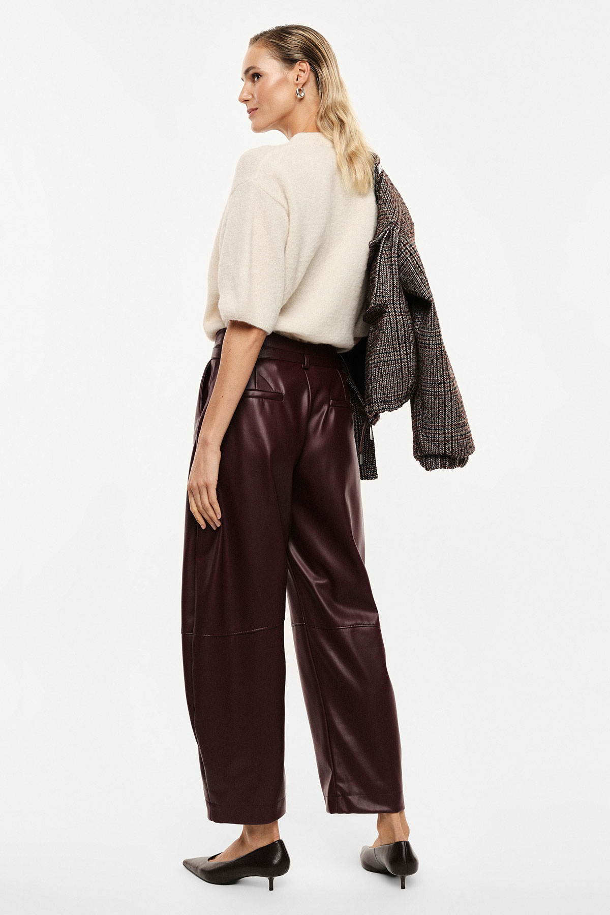 Female model from behind wearing cream short-sleeve sweater, burgundy leather wide-leg trousers and black kitten heels, tweed jacket draped over shoulder