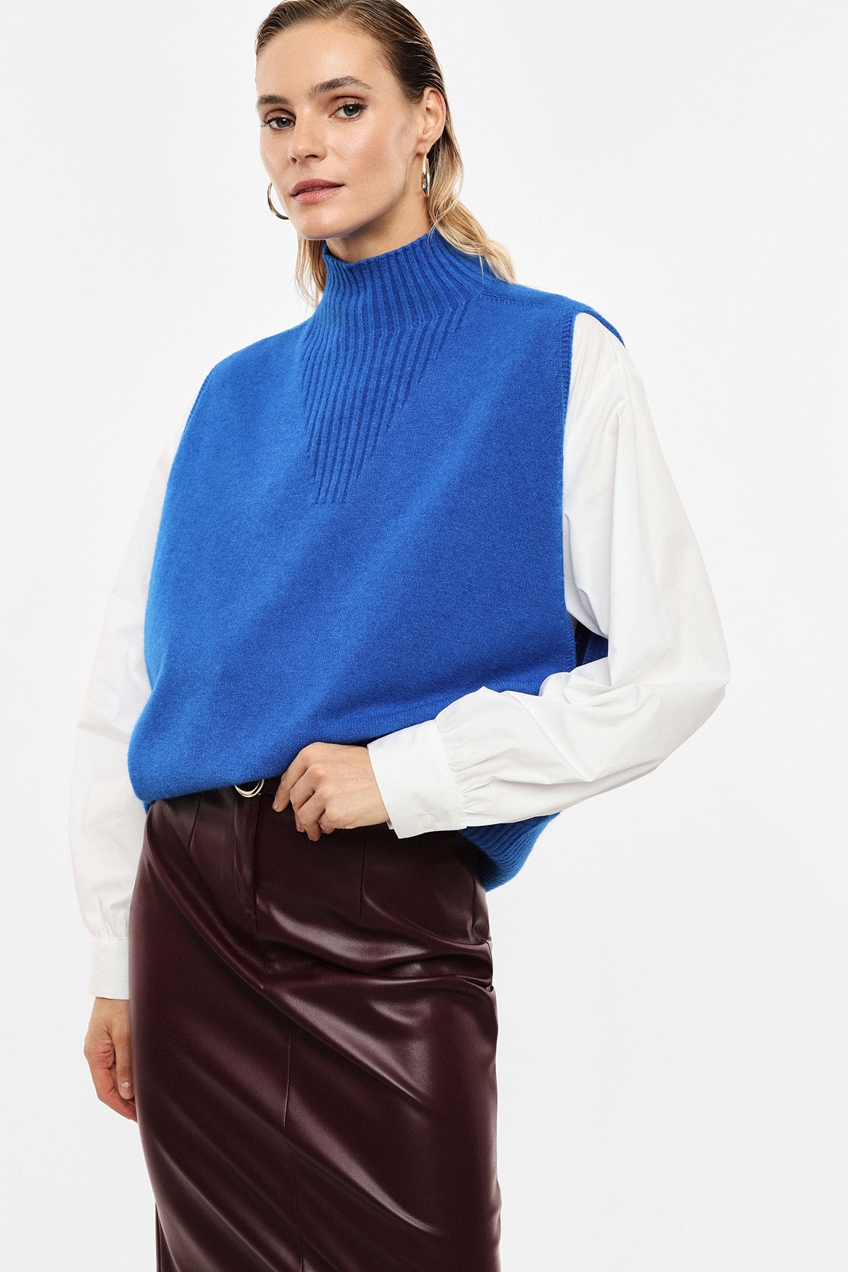 Woman modelling cobalt blue knitted sleeveless vest layered over white blouse with burgundy leather pencil skirt