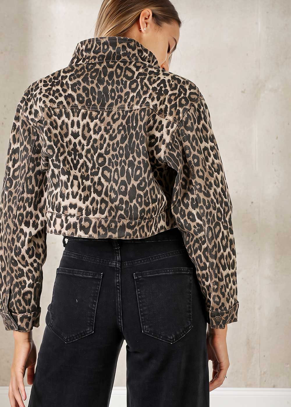 Woman wearing cropped leopard-print denim jacket viewed from back with high-waist black jeans against neutral wall