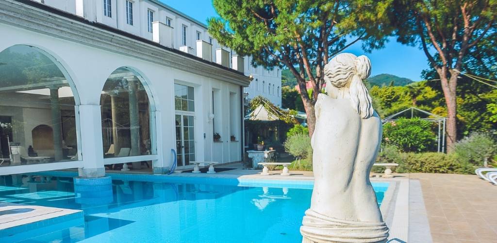 White marble statue of a female figure beside a clear blue swimming pool at a Mediterranean villa with trees and terraces