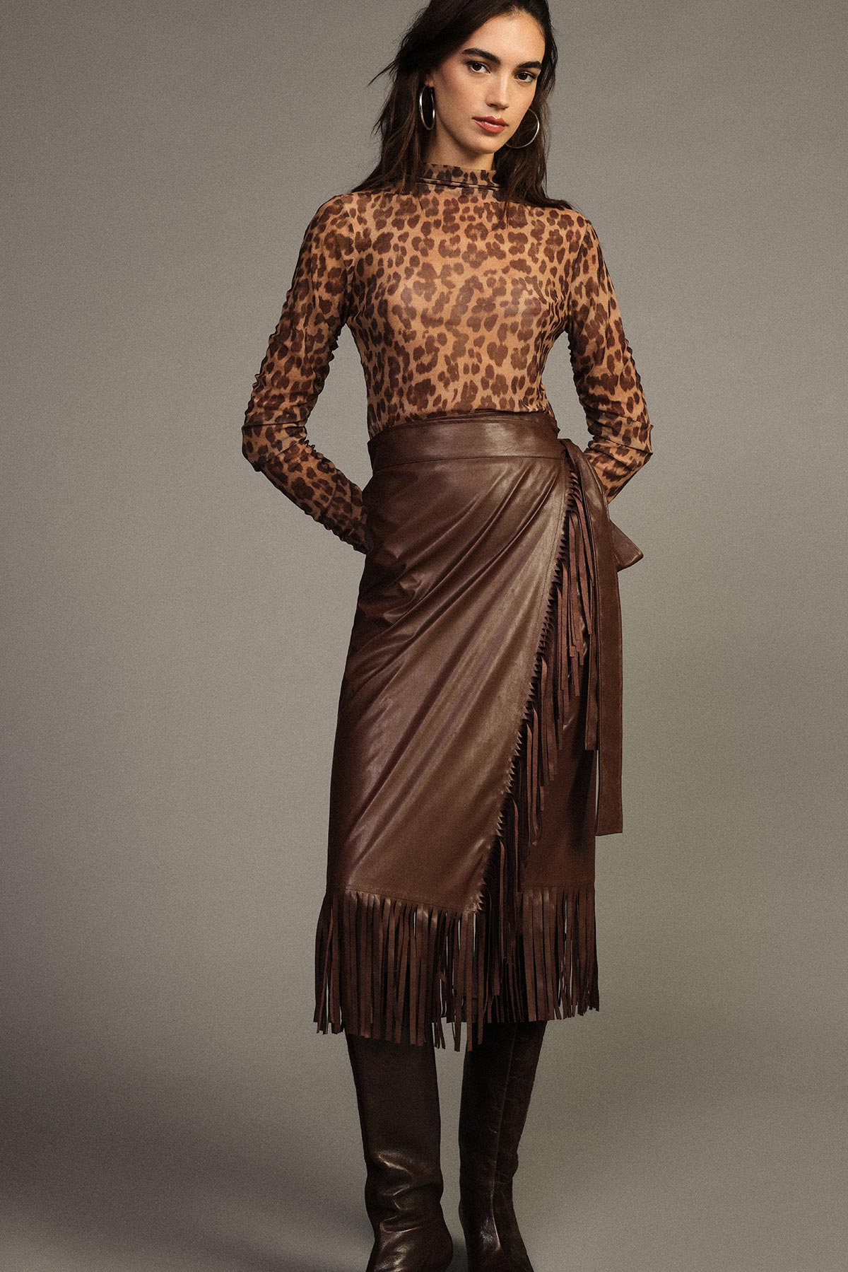 Woman modelling brown leopard-print sheer top with wrap leather fringe midi skirt and knee-high boots in studio