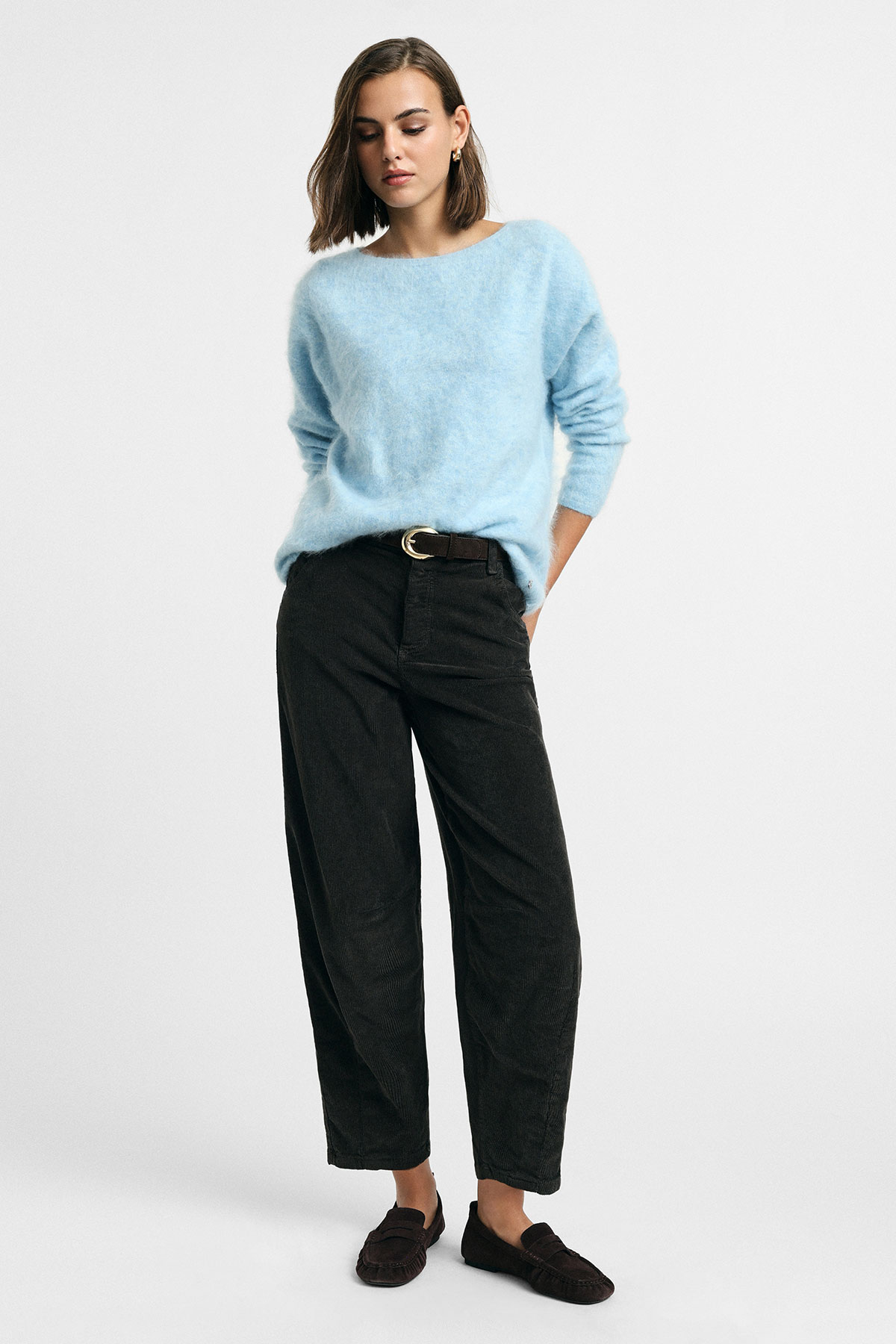 Model wearing a pale blue fluffy sweater with black wide-leg trousers, belt and dark loafers on white background