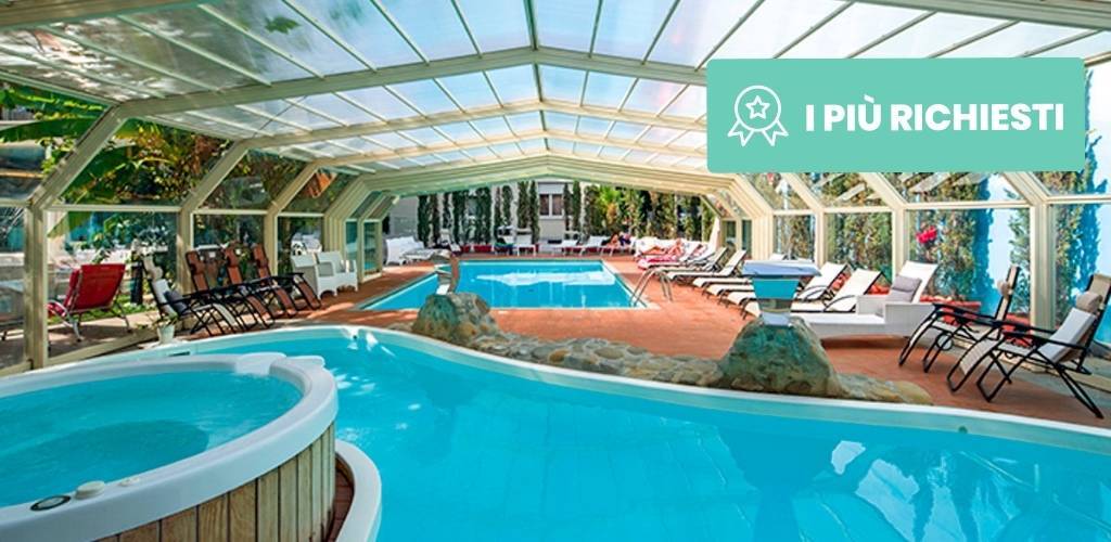 Covered indoor resort pool and hot tub with sun loungers and glass roof in a landscaped spa area