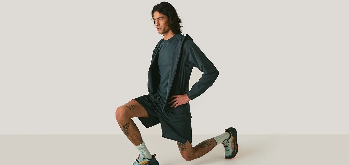 Atleta in abbigliamento sportivo blu scuro, composto da una maglietta a maniche lunghe, pantaloni corti e scarpe da ginnastica multicolori, che sta eseguendo un affondo.