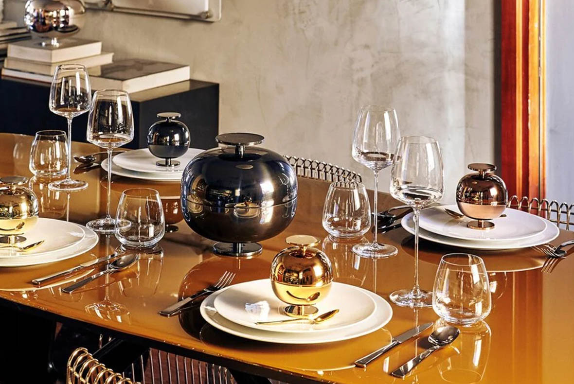 Modern glossy gold dining table set with white plates, wine glasses, polished cutlery and reflective metallic orb centrepieces