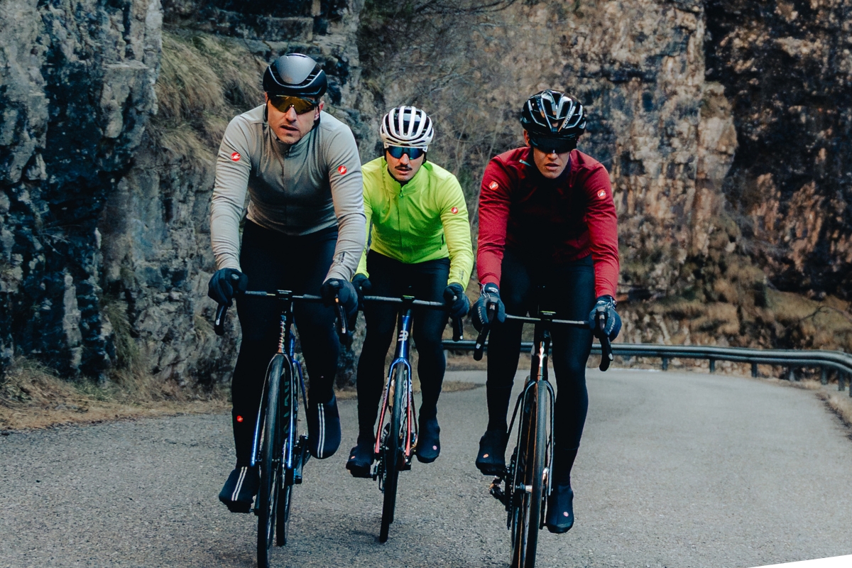 Three cyclists in helmets and bright jackets riding road bikes on a winding mountain road by rocky cliffs