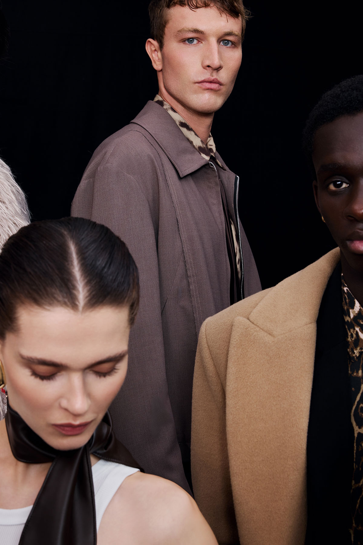 Three diverse fashion models in autumn coats and patterned shirts against a black background, close-up portrait with neutral expressions