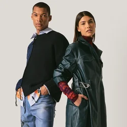 Uomo e donna in piedi schiena contro schiena, vestiti con abiti moderni a strati con denim, trench in pelle e scarpe casual su sfondo neutro.