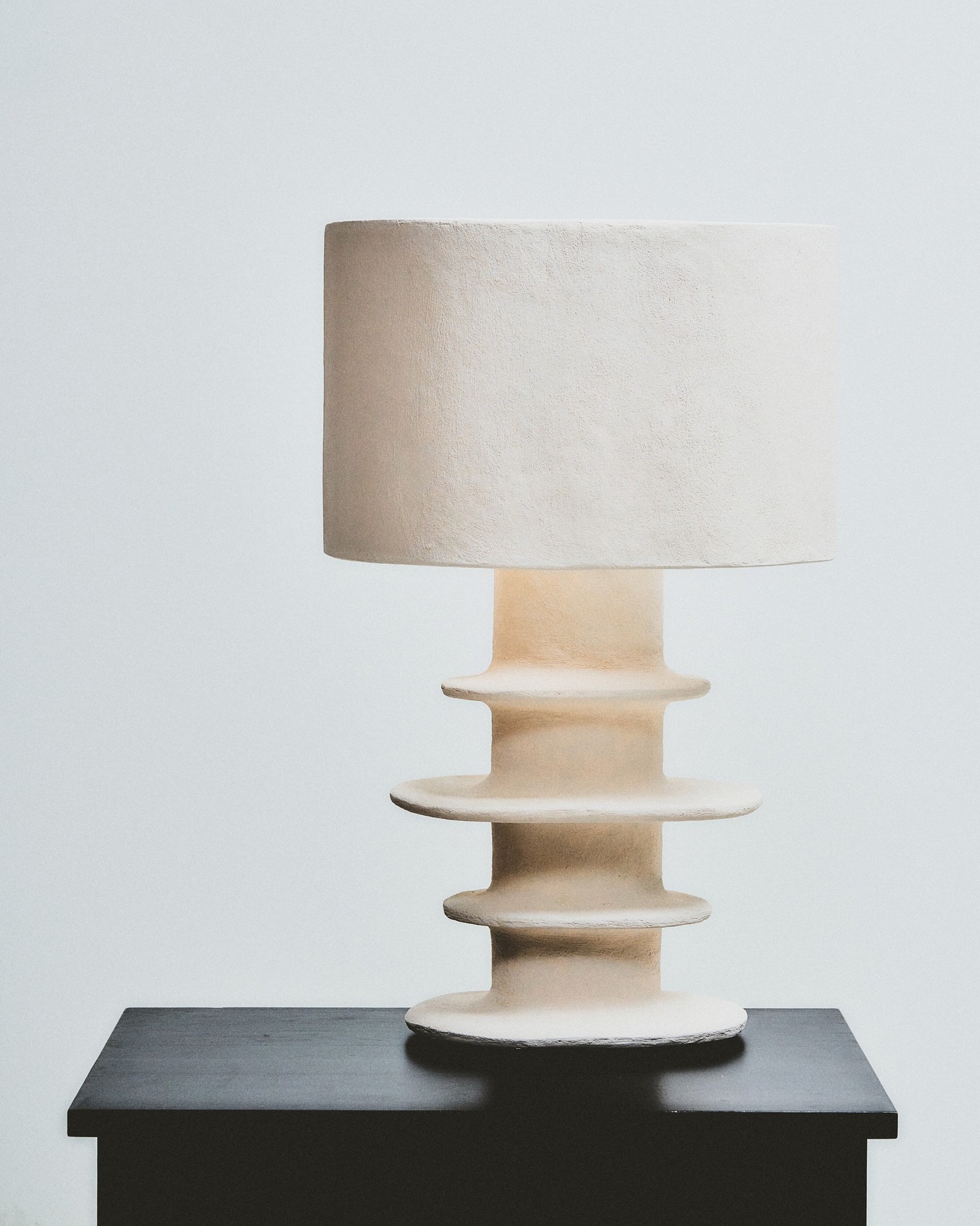 Cream textured table lamp with sculptural stacked-disk ceramic base and drum shade on a black side table