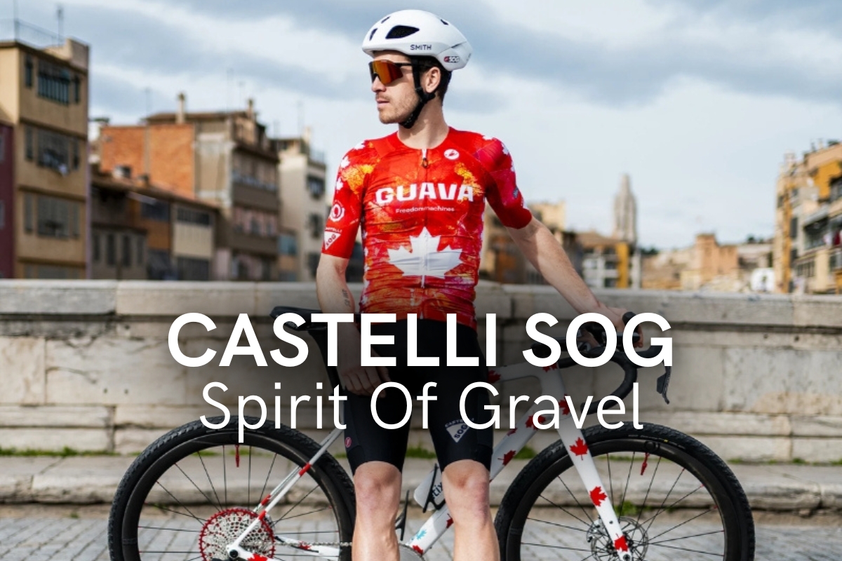 Cyclist in red GUAVA jersey and white helmet standing with a Castelli SOG gravel bike on a city bridge with urban buildings in the background
