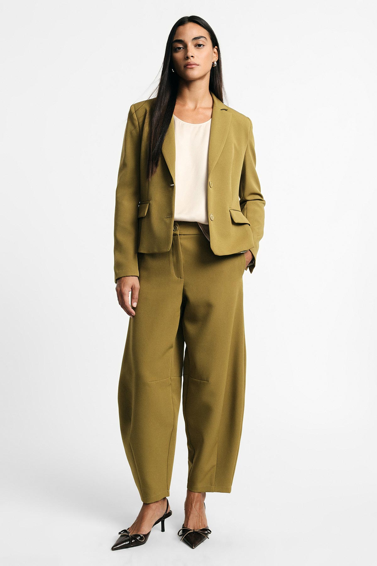 Woman standing in olive-green women's suit with wide-leg trousers, matching blazer, cream blouse and black pointed heels