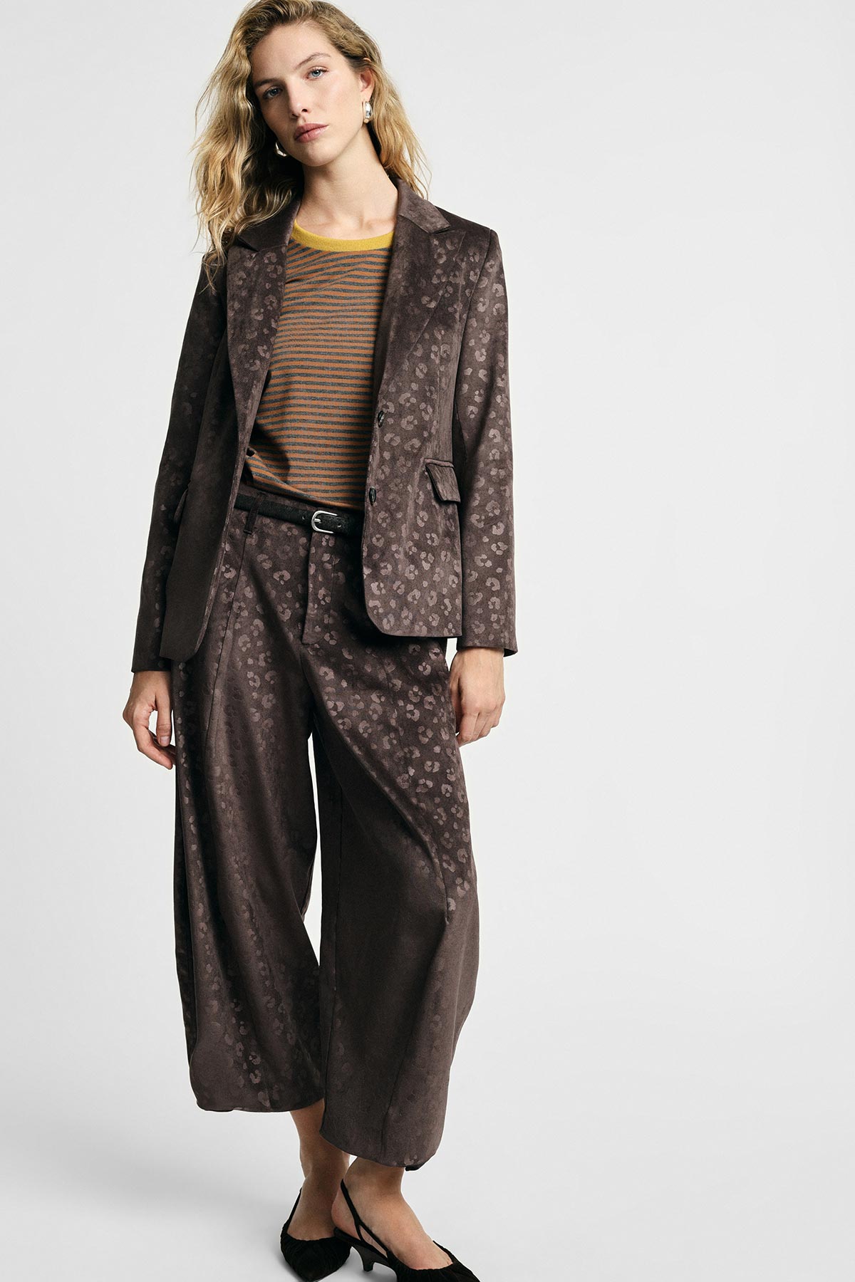 Female model in brown jacquard blazer and wide-leg trousers, striped knit top and black slingback heels, standing