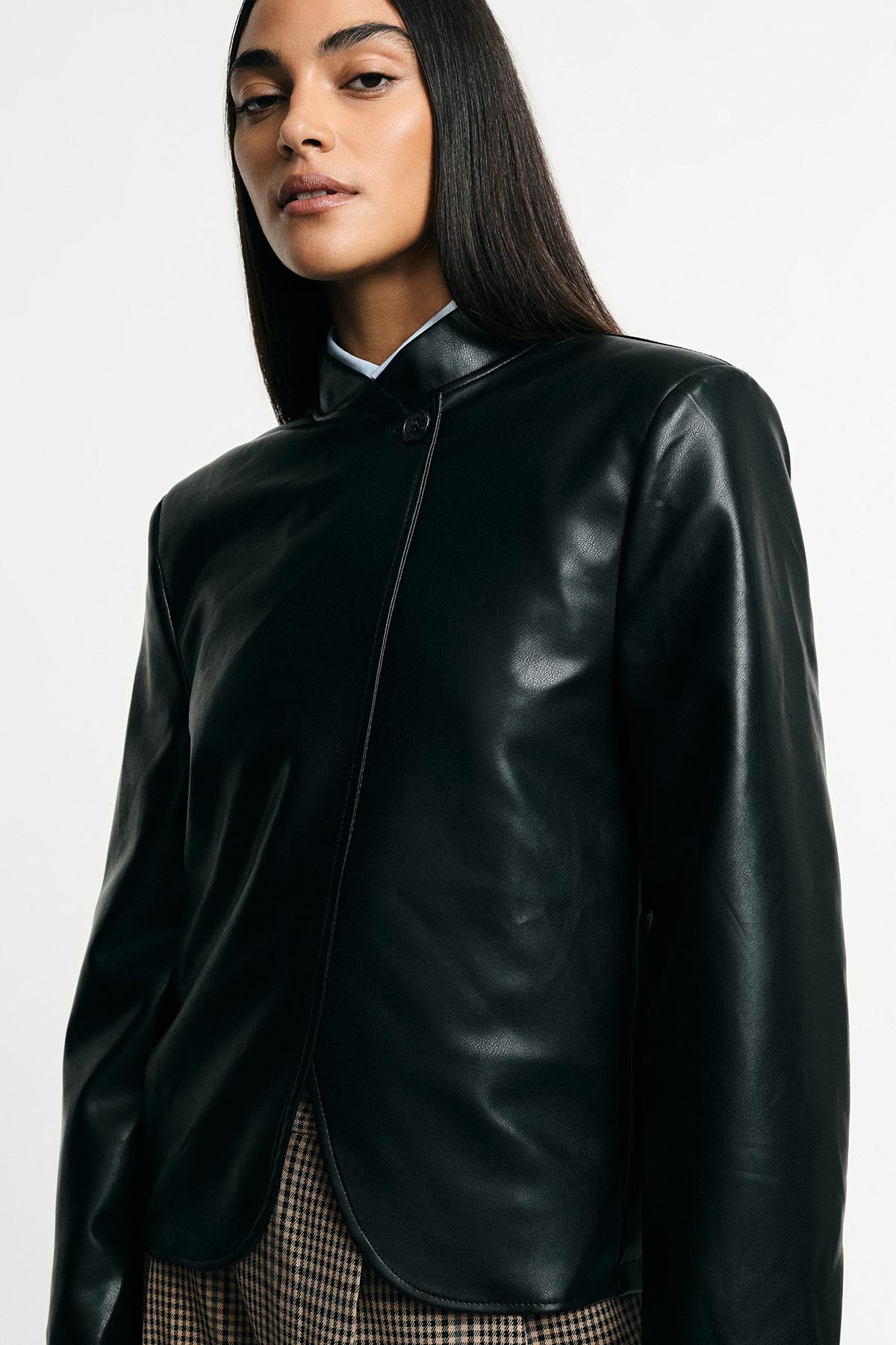 Woman wearing black leather jacket with mandarin collar and single button, paired with checked trousers, studio portrait