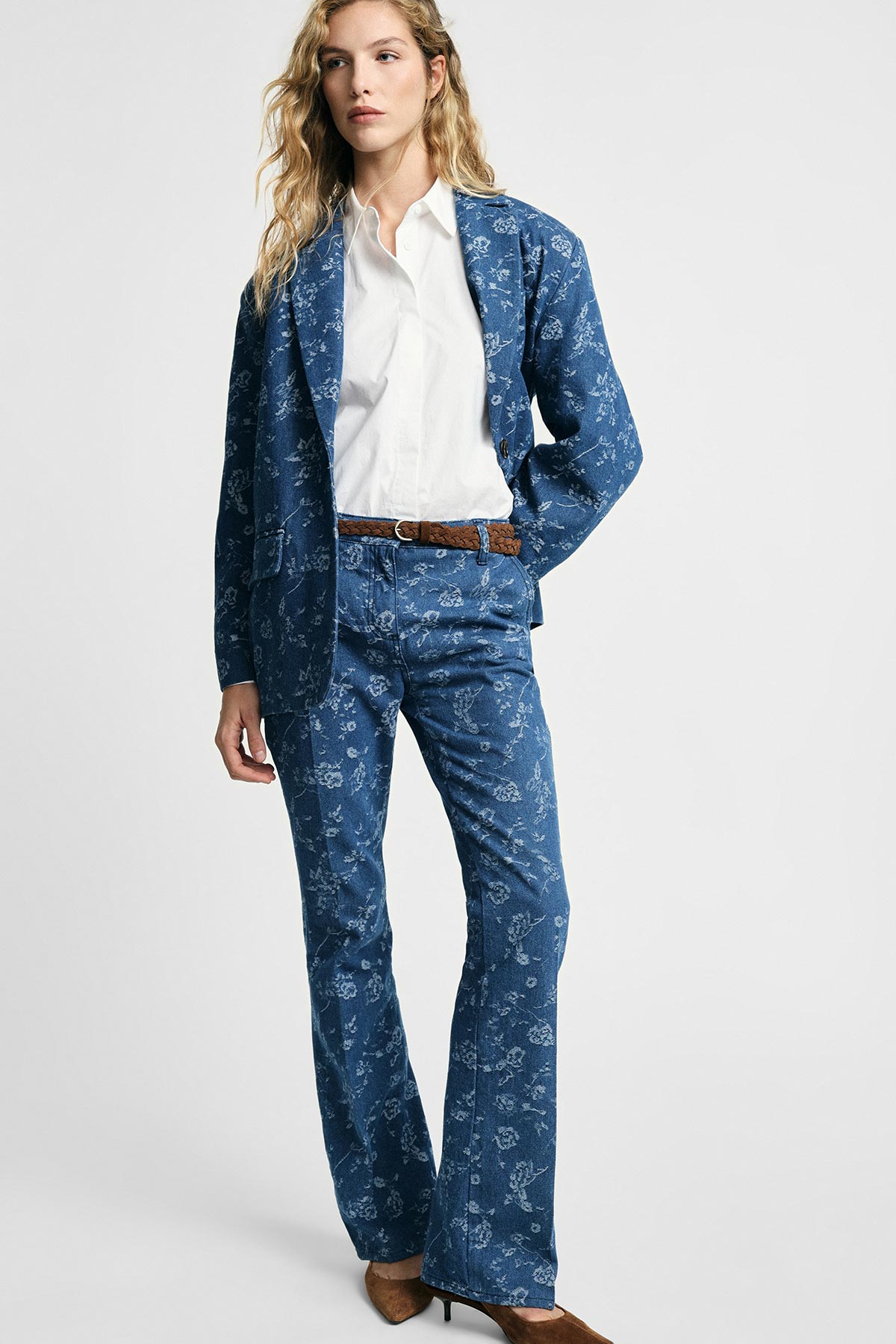 Female model wearing blue floral patterned blazer and flared trousers with white shirt, brown belt and heels