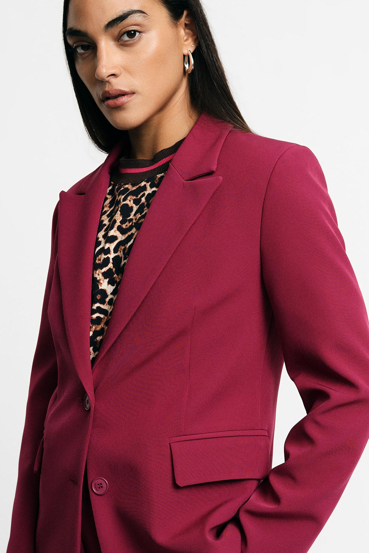 Woman wearing magenta blazer over leopard-print top with hoop earring and hand in pocket, cropped studio portrait