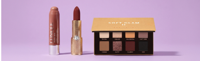 Una matita per il make-up, un rossetto e una palette di ombretti su uno sfondo viola.