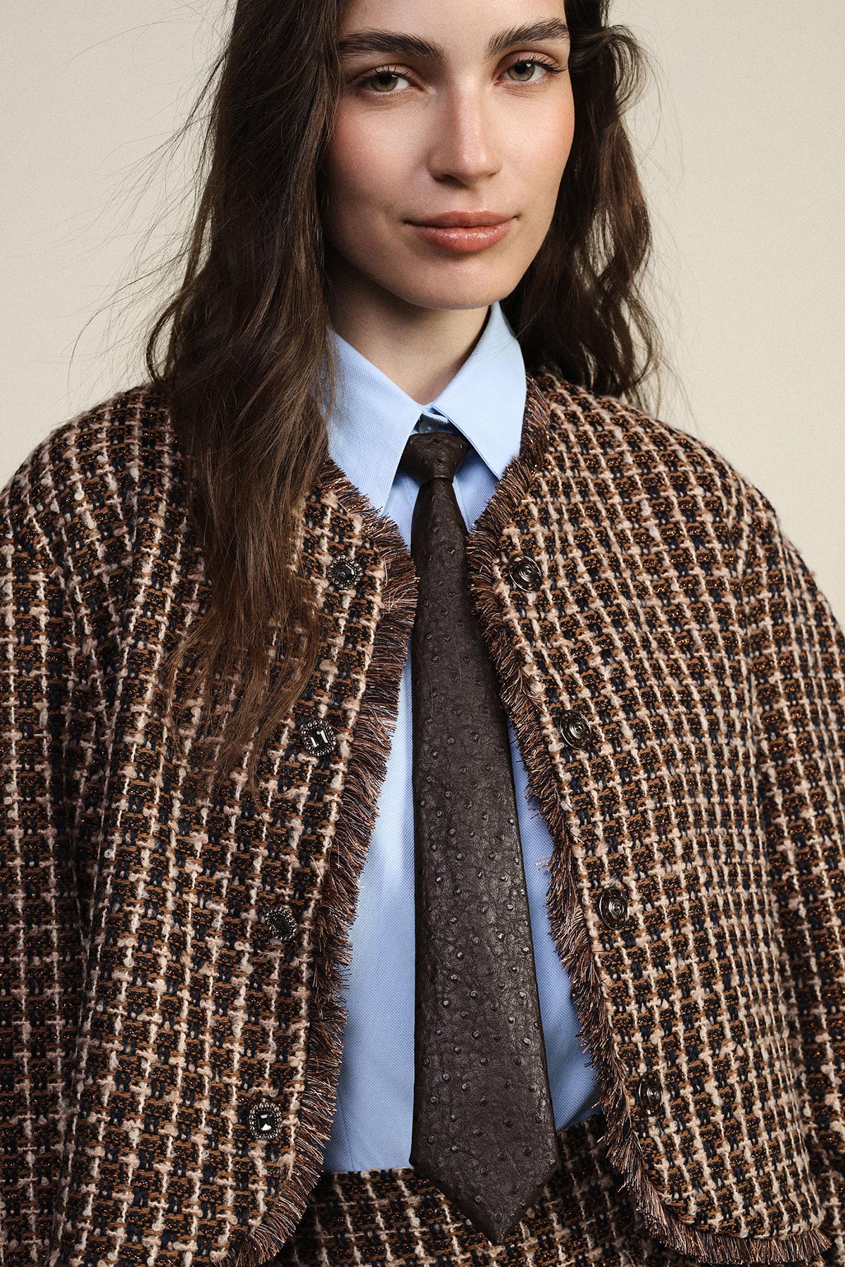 Close-up portrait of a young woman wearing a brown tweed jacket, light blue shirt and textured brown tie