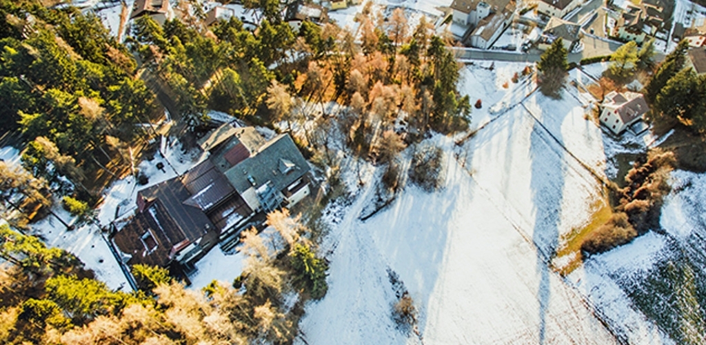 Aerial view of a small snowy village with houses, evergreen and deciduous trees casting long winter shadows