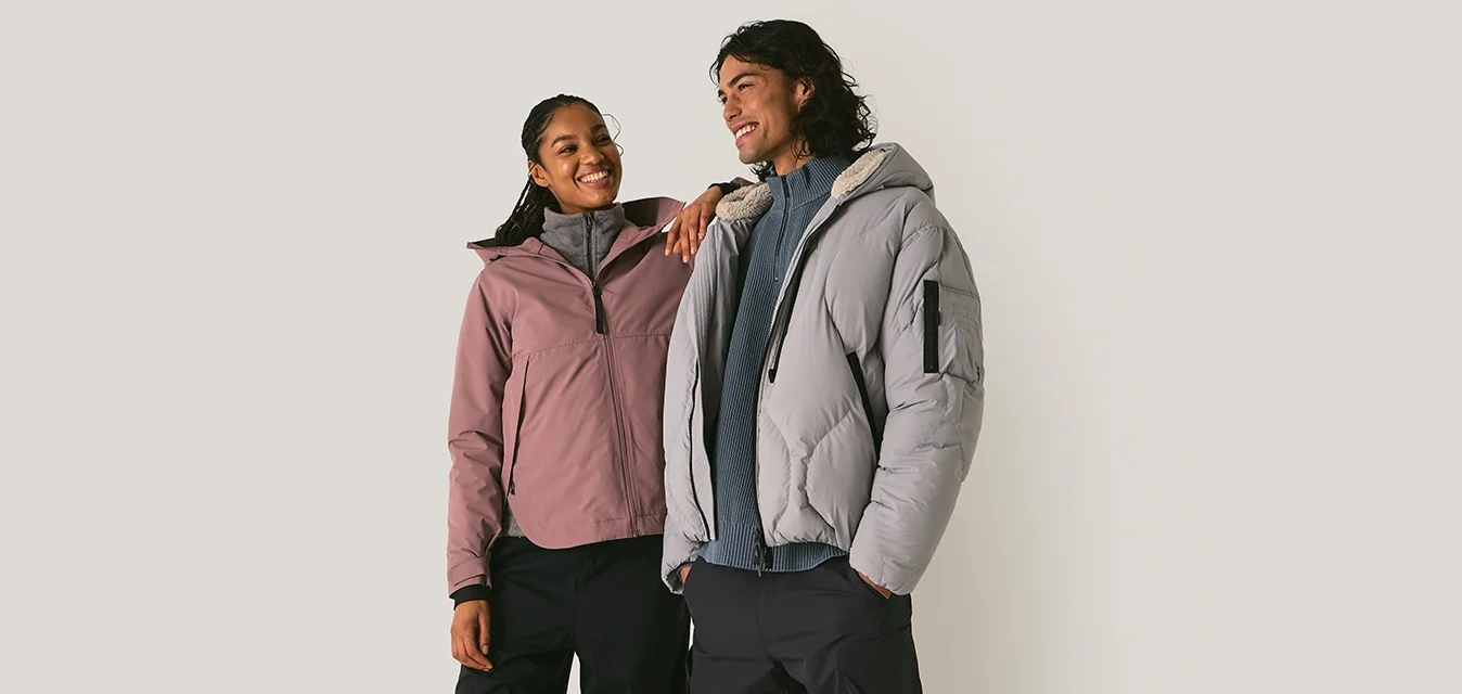 Due persone in abbigliamento da esterno: una con una giacca rosa chiaro, l'altra con un piumino grigio; entrambe con pantaloni neri e scarpe casual.