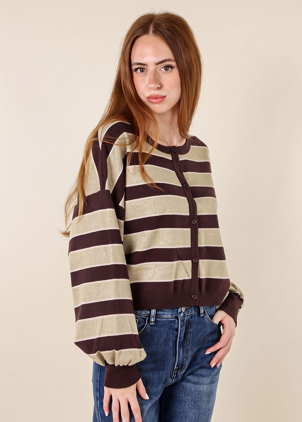 Young woman modelling brown and beige striped button-up cardigan with balloon sleeves and blue jeans on a neutral background