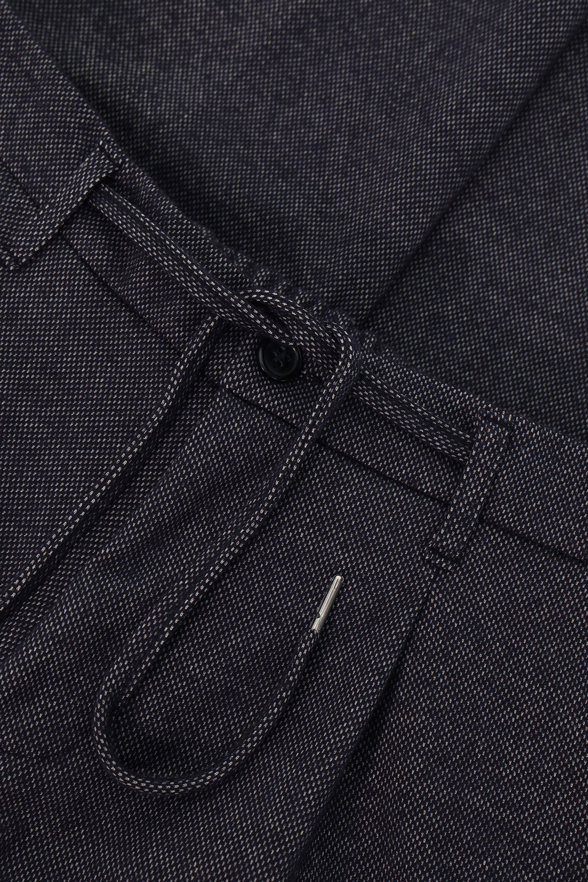 Close-up of dark indigo denim trousers waistband showing textured fabric, button, belt loop and drawstring with metal aglet