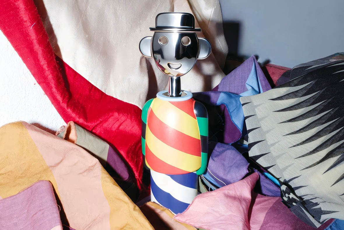 Smiling chrome-capped corkscrew with colourful diagonal-striped body placed among folded patterned fabrics